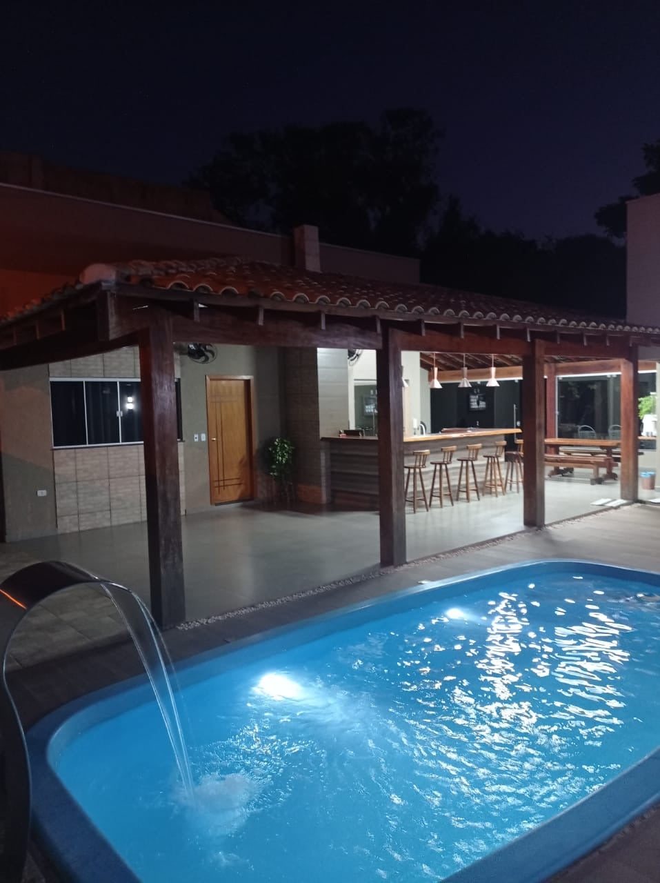 Piscina iluminada e área gourmet do Pesqueiro Lazer City ao anoitecer